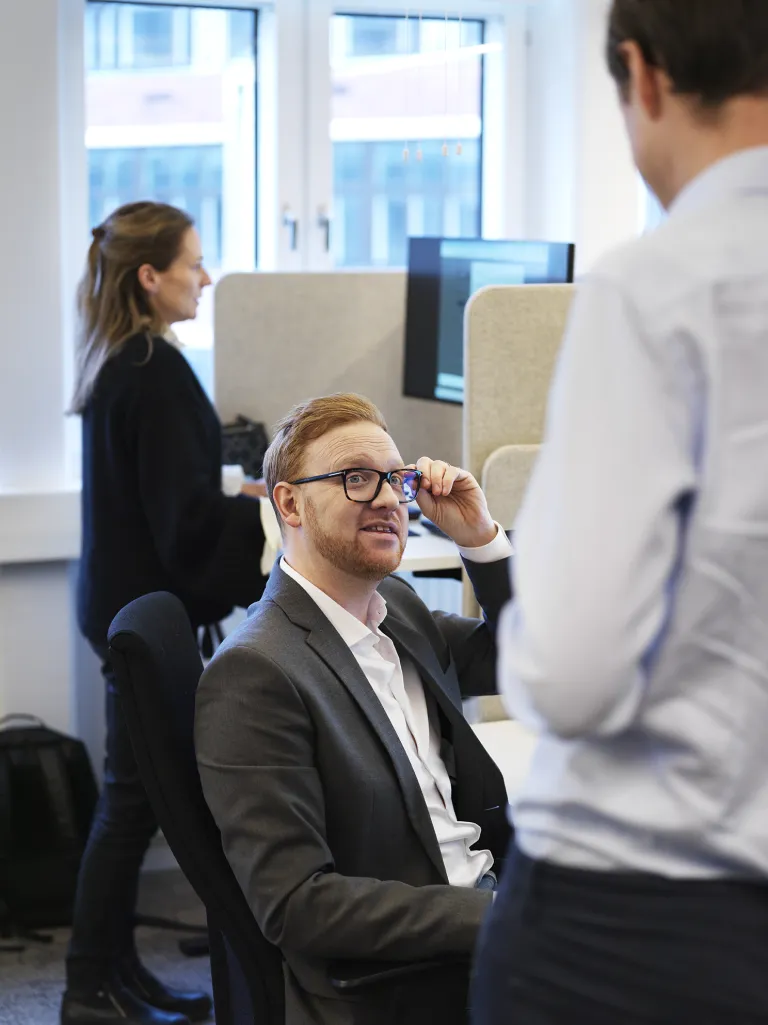 Kolleger i samtale ved stående skriveborde på et lyst kontor